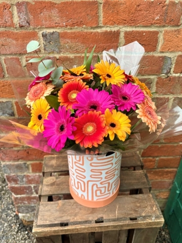 A bright and colourful germini flower arrangement in shades of pink, orange, and yellow, presented in a modern patterned gift box.